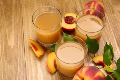 Glasses of peach juice, fresh fruits and leaves on wooden table