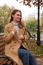 Photo of Beautiful young woman wearing stylish clothes on bench in autumn park