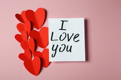 Photo of Paper hearts and card with phrase I LOVE YOU on pink background, flat lay