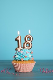 Photo of 18th birthday. Delicious cupcake with number shaped candles for coming of age party on light blue wooden table