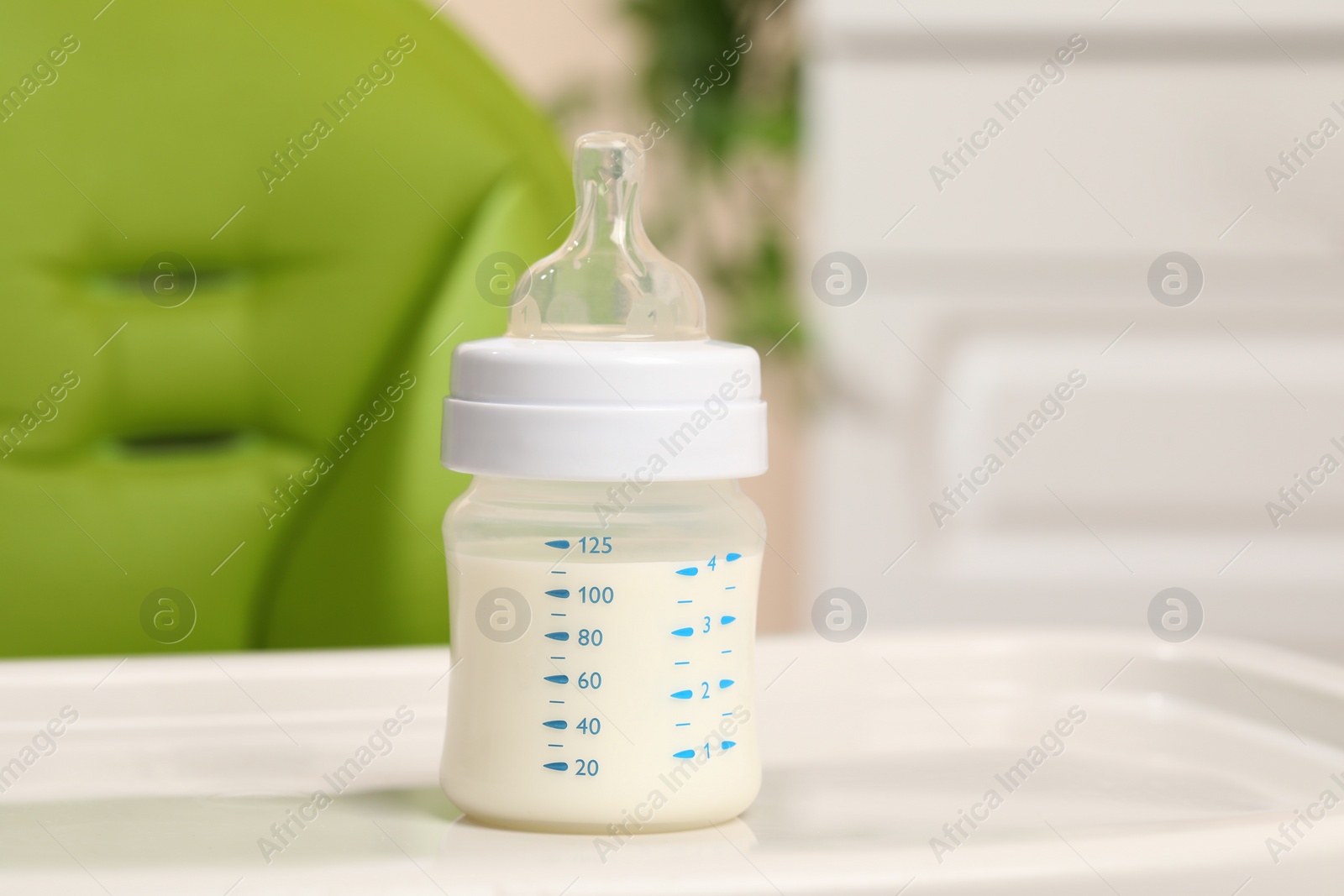 Photo of High chair with feeding bottle of infant formula on white tray indoors
