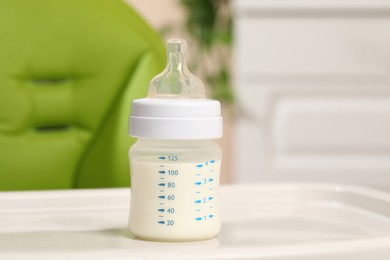 High chair with feeding bottle of infant formula on white tray indoors