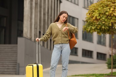 Photo of Being late. Worried woman with suitcase and backpack looking at watch outdoors