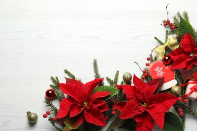 Photo of Flat lay composition with poinsettias (traditional Christmas flowers) and holiday decor on white wooden table. Space for text