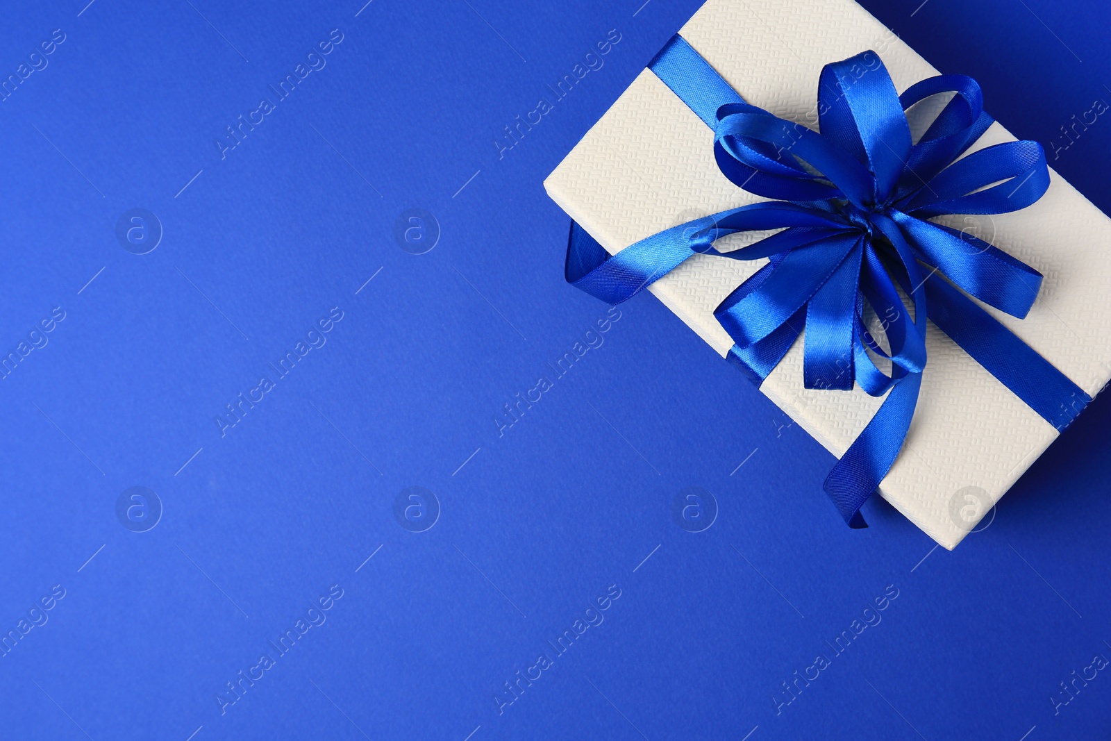 Photo of Beautiful gift box with bow on blue background, top view. Space for text