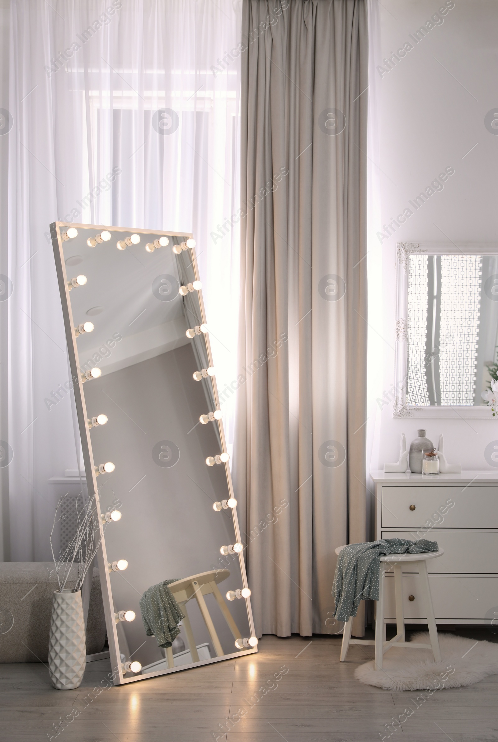 Photo of Large mirror with light bulbs and chest of drawers in stylish room. Interior design