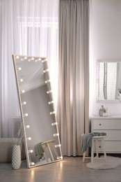 Large mirror with light bulbs and chest of drawers in stylish room. Interior design