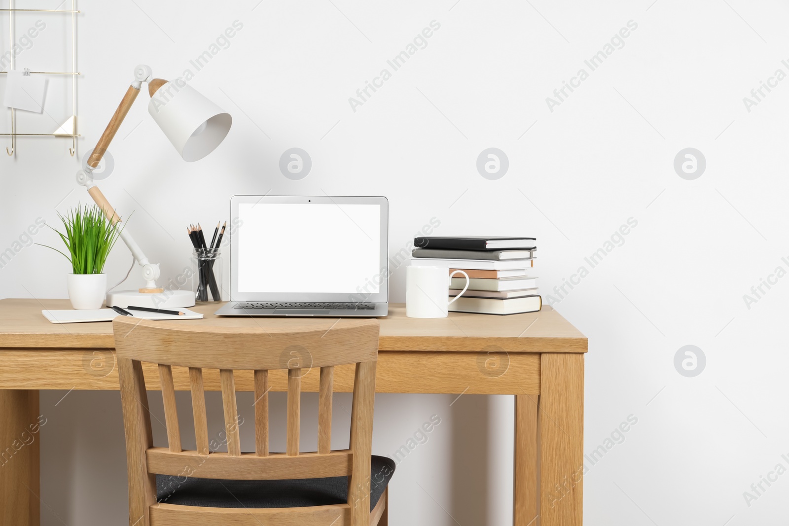 Photo of Cozy workspace with laptop, lamp and stationery on wooden desk at home