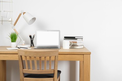 Cozy workspace with laptop, lamp and stationery on wooden desk at home