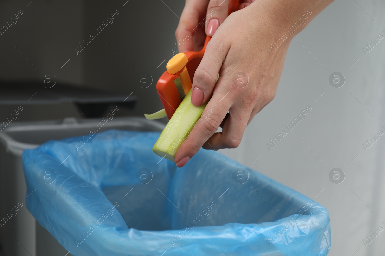 Photo of Woman peeling fresh zucchini above garbage bin indoors, closeup