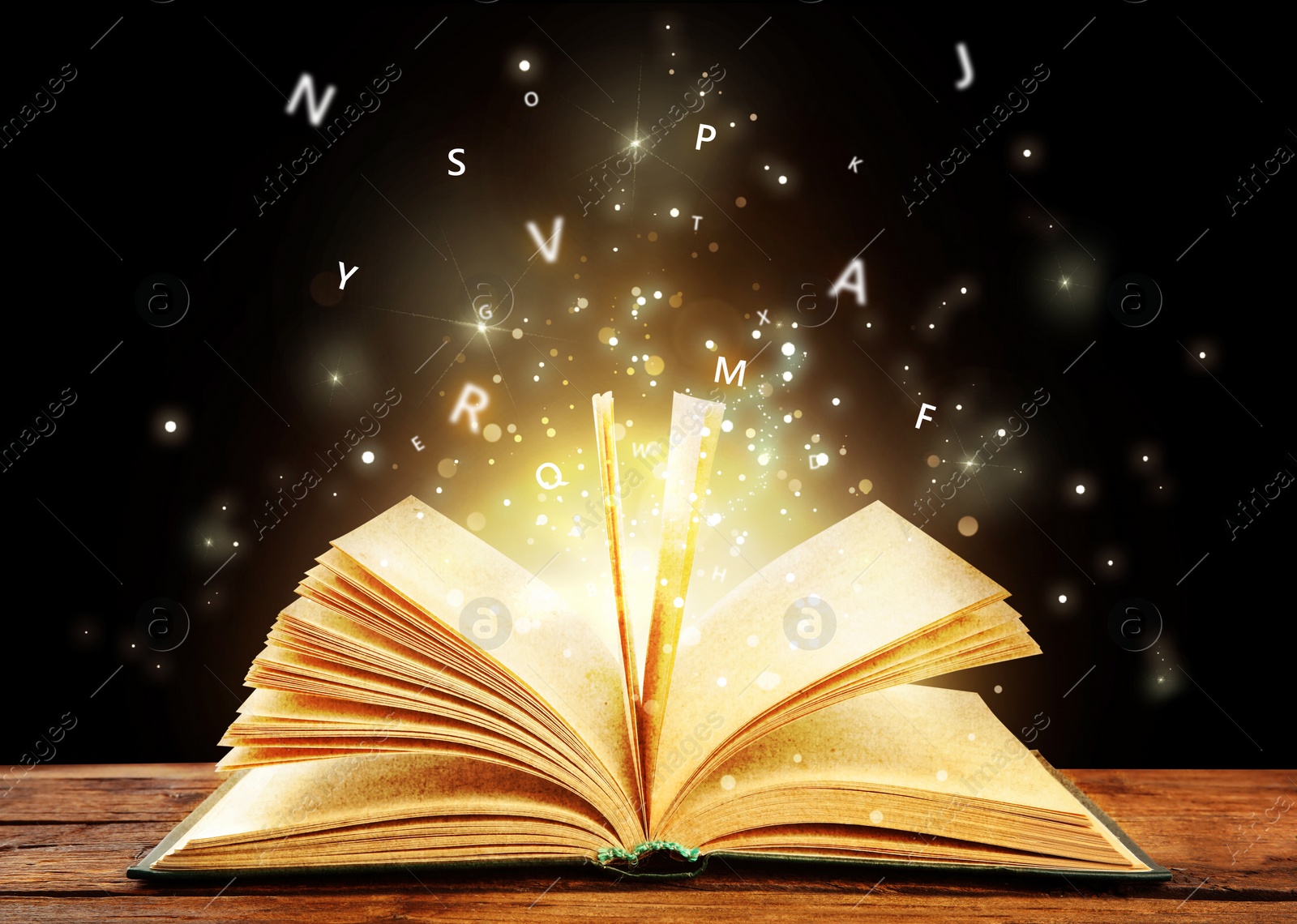 Image of Open book with magic light and glowing letters flying out of it on wooden table against black background