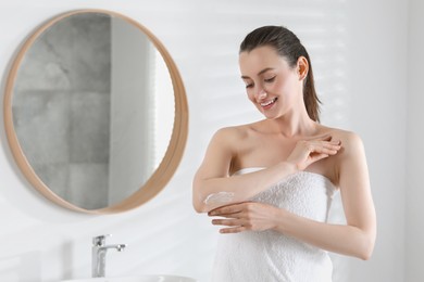 Photo of Happy woman applying body cream onto elbow in bathroom, space for text