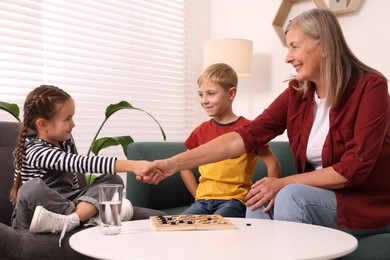 Family playing checkers at coffee table in room. Grandmother shaking hands with her nephew after game