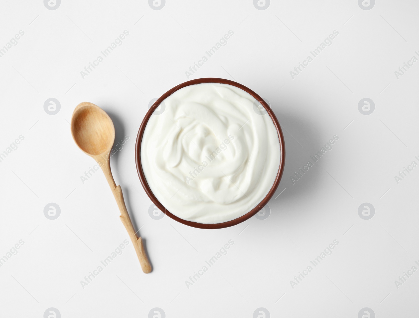 Photo of Bowl of sour cream and wooden spoon on white background, top view