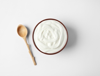 Bowl of sour cream and wooden spoon on white background, top view