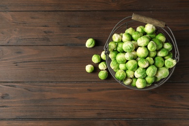 Photo of Metal basket with fresh Brussels sprouts on wooden background, top view. Space for text