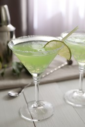 Delicious Margarita cocktail in glasses and lime on white wooden table