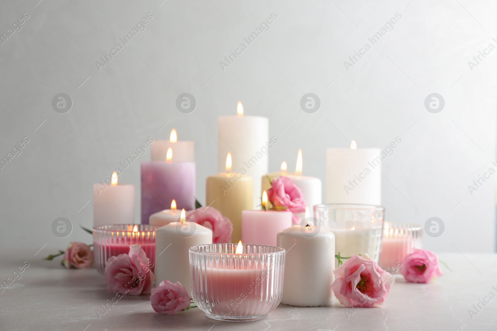 Photo of Composition with burning candles on table against light background