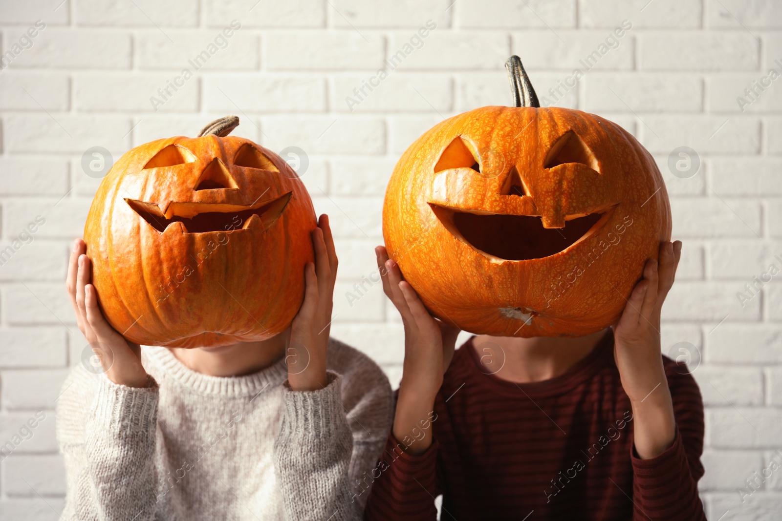 Photo of Women holding Halloween pumpkin head jack lanterns against brick wall