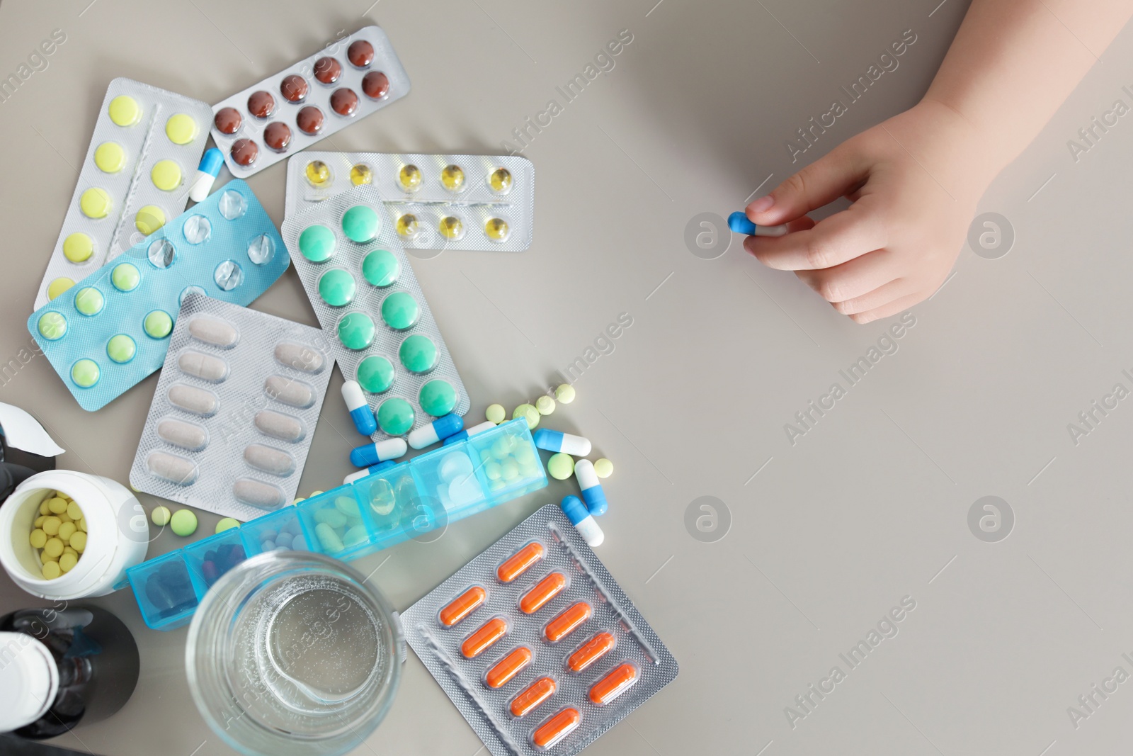 Photo of Little child with many different pills at table, top view. Danger of medicament intoxication