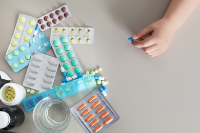 Photo of Little child with many different pills at table, top view. Danger of medicament intoxication