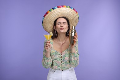 Photo of Young woman in Mexican sombrero hat with cocktail and shaker sending air kiss on violet background