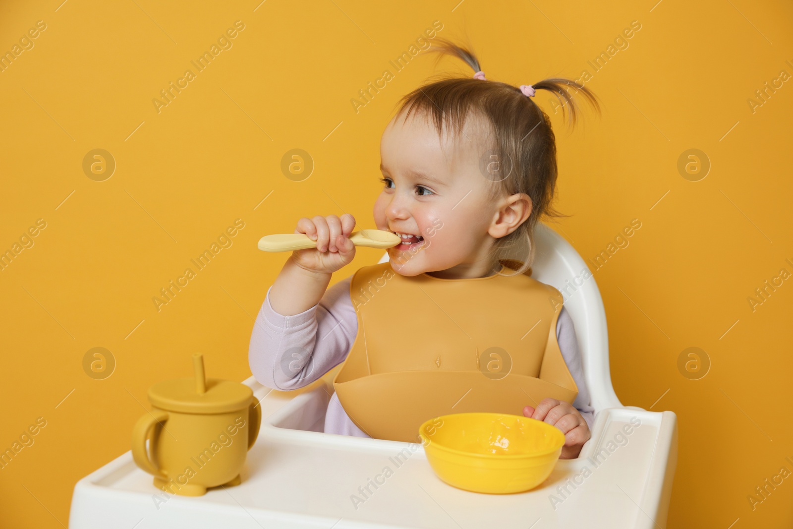 Photo of Cute little baby wearing bib while eating on yellow background