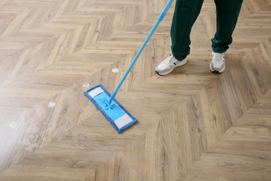 Photo of Professional janitor cleaning parquet floor with mop, closeup