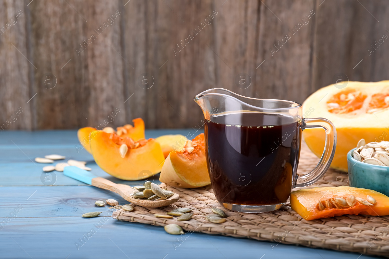 Photo of Fresh pumpkin seed oil in glass pitcher on blue wooden table. Space for text