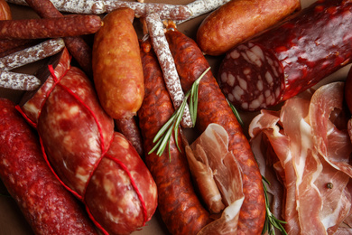 Different types of sausages with rosemary as background, flat lay