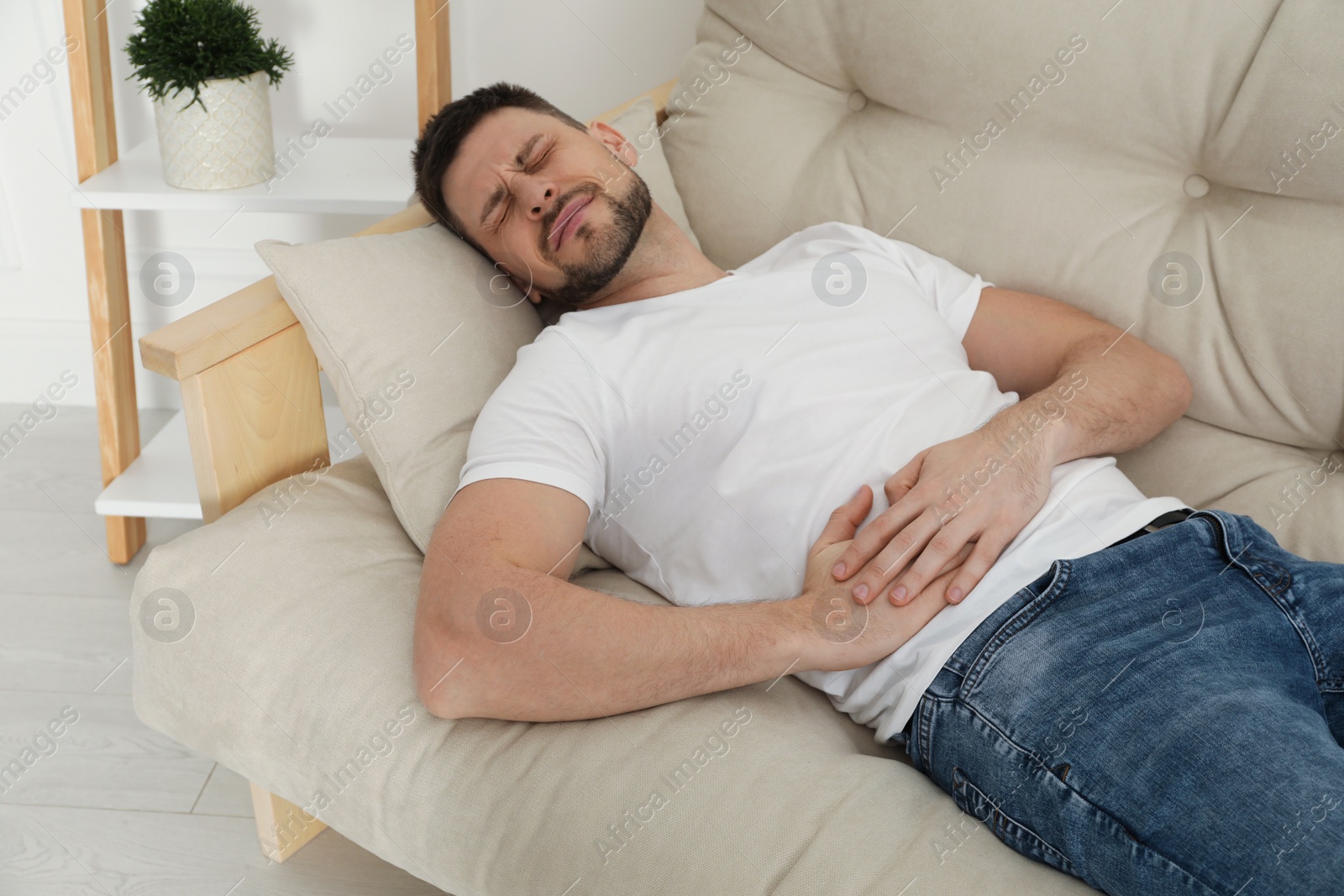 Photo of Man suffering from pain in lower right abdomen on sofa at home. Acute appendicitis