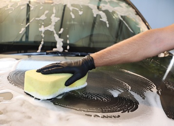 Photo of Worker cleaning automobile with sponge at car wash, closeup