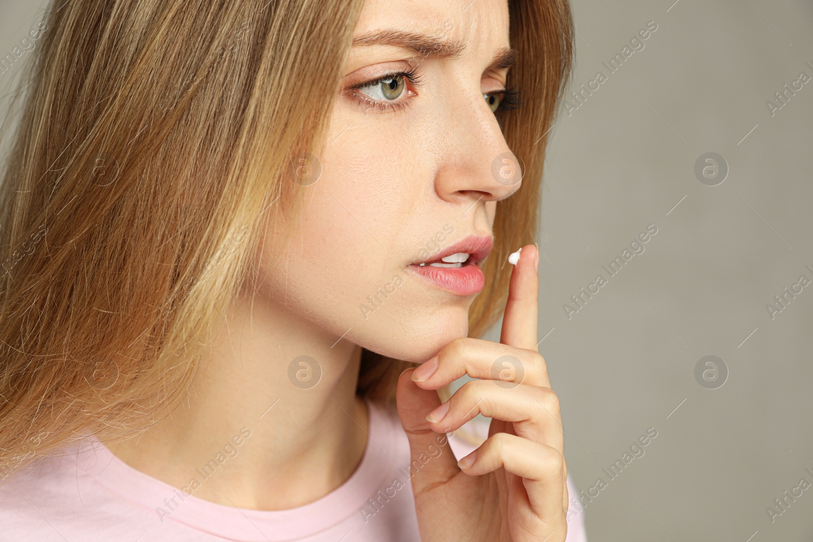 Photo of Woman with herpes applying cream onto lip against  light grey background