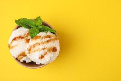 Scoops of tasty ice cream with caramel sauce and mint on yellow background, top view. Space for text