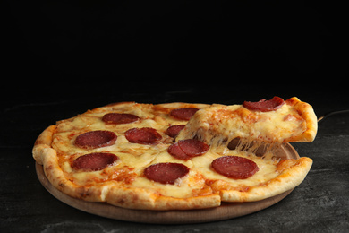 Photo of Taking slice of tasty pepperoni pizza on black table