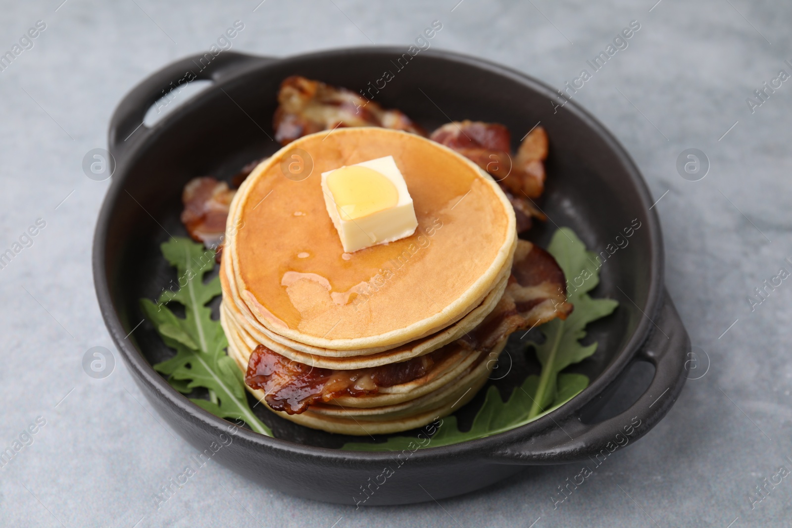 Photo of Tasty pancakes with butter, fried bacon and fresh arugula on grey table