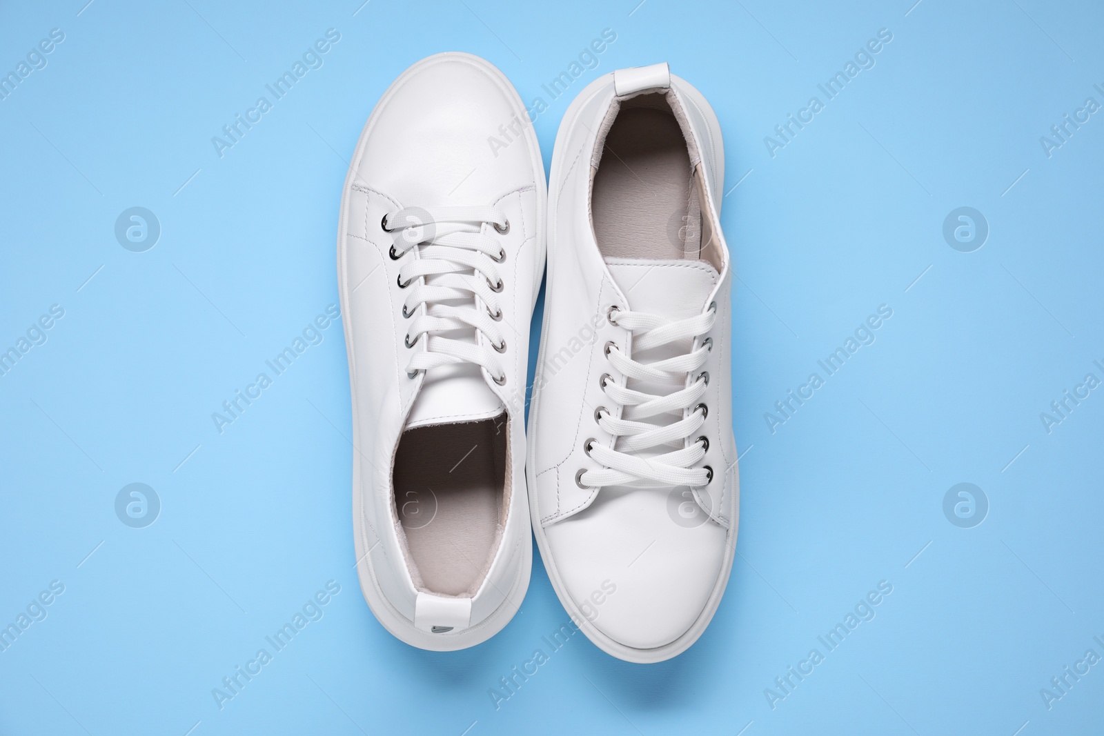 Photo of Pair of stylish white sneakers on light blue background, top view