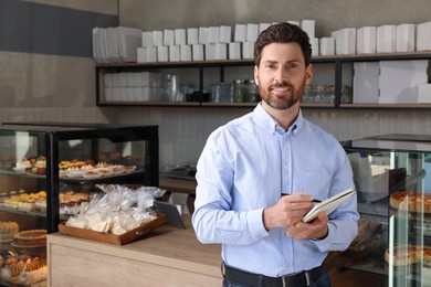 Photo of Happy business owner with notebook and pen in bakery shop