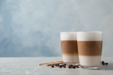 Photo of Glasses of delicious layered coffee, beans and straws on grey marble table against light background, space for text