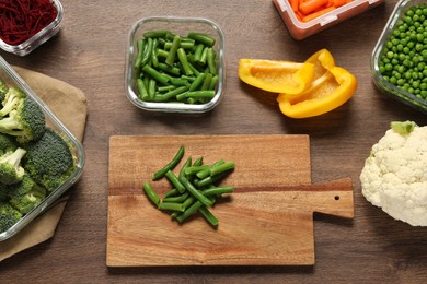 Photo of Wooden board with green beans and containers with fresh products on wooden table, flat lay. Food storage