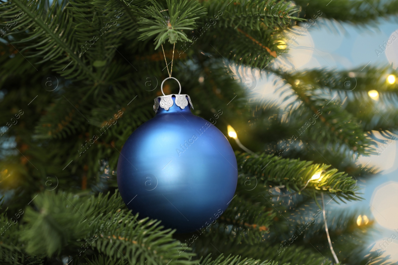 Photo of Beautiful blue bauble hanging on Christmas tree against blurred festive lights, closeup