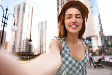 Beautiful young woman in stylish hat taking selfie outdoors