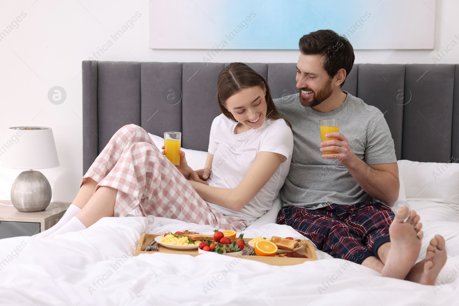 Photo of Happy couple eating tasty breakfast on bed at home