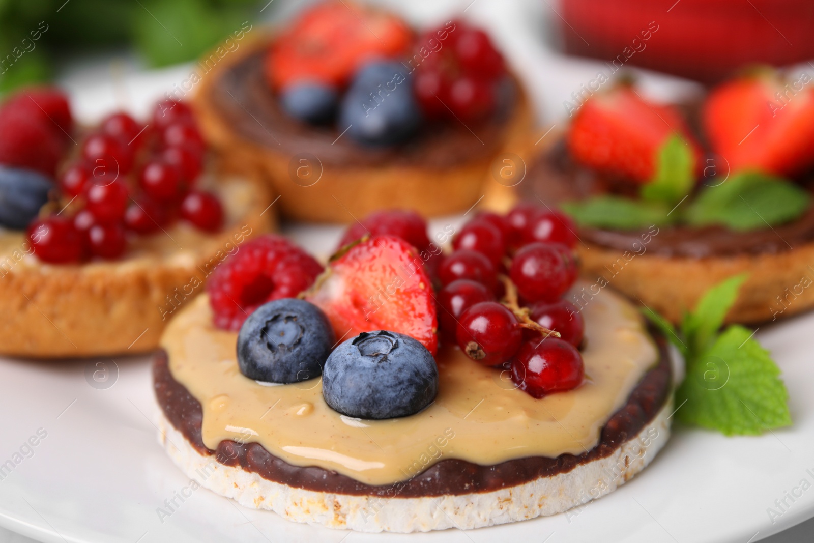 Photo of Fresh rice cake and rusks with different toppings served on white plate, closeup