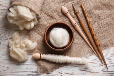 Photo of Soft wool and spindles on white wooden table, flat lay