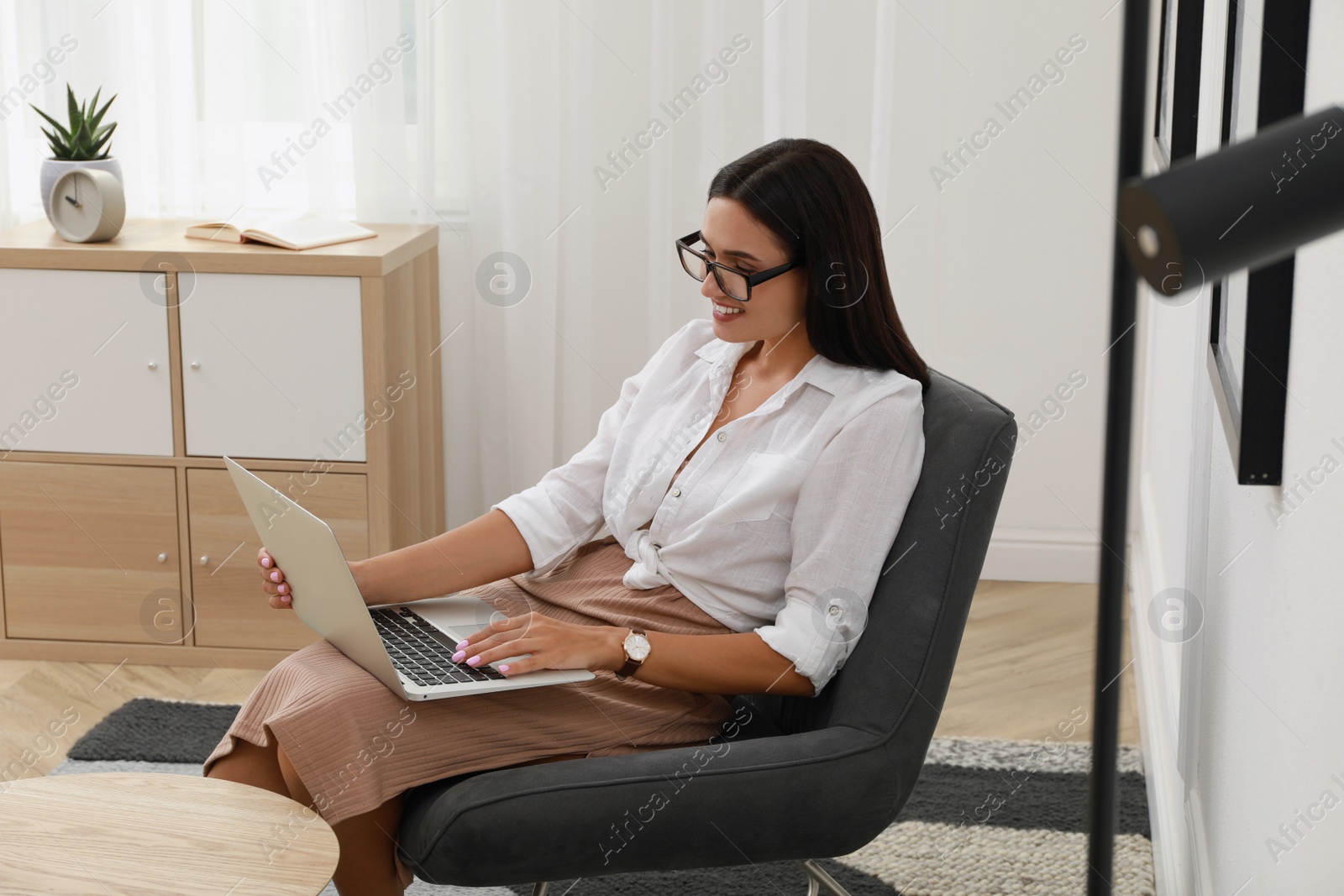 Photo of Young woman using laptop in armchair at home. Internet shopping