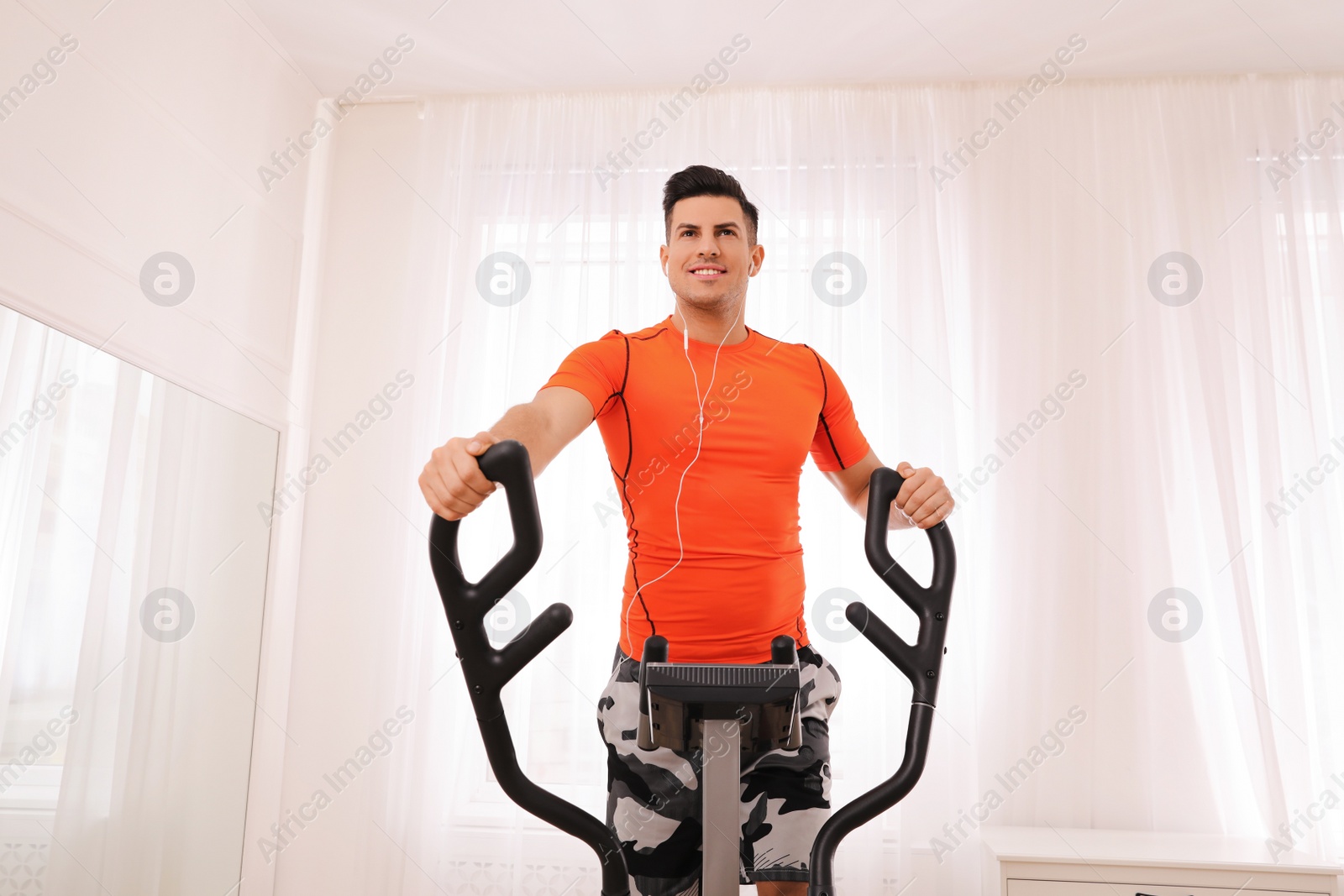 Photo of Man using modern elliptical machine at home