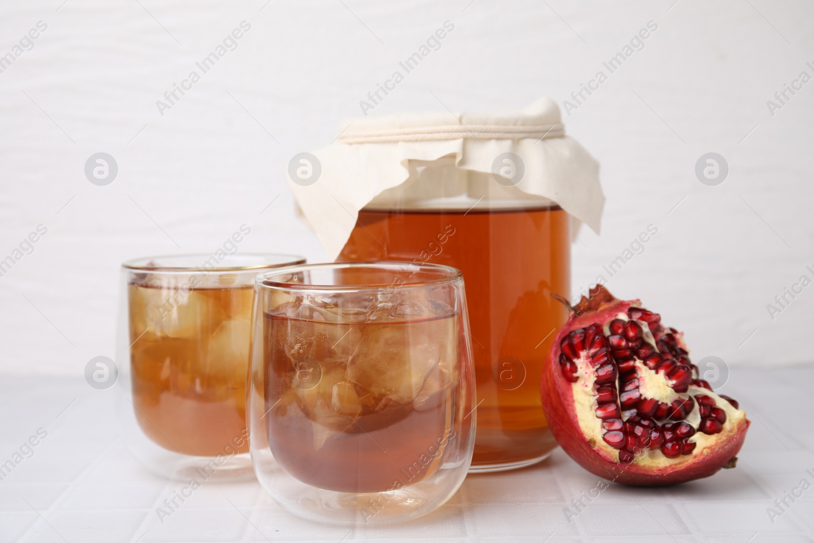Photo of Tasty kombucha with ice cubes and pomegranate on white tiled table