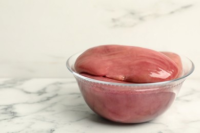 Photo of Bowl with fresh raw pork kidneys on white marble table, space for text