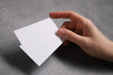 Photo of Woman holding blank cards at grey table, closeup. Mockup for design